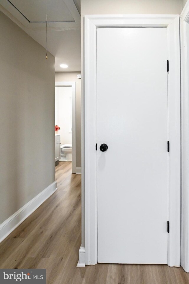 hall featuring attic access, wood finished floors, and baseboards