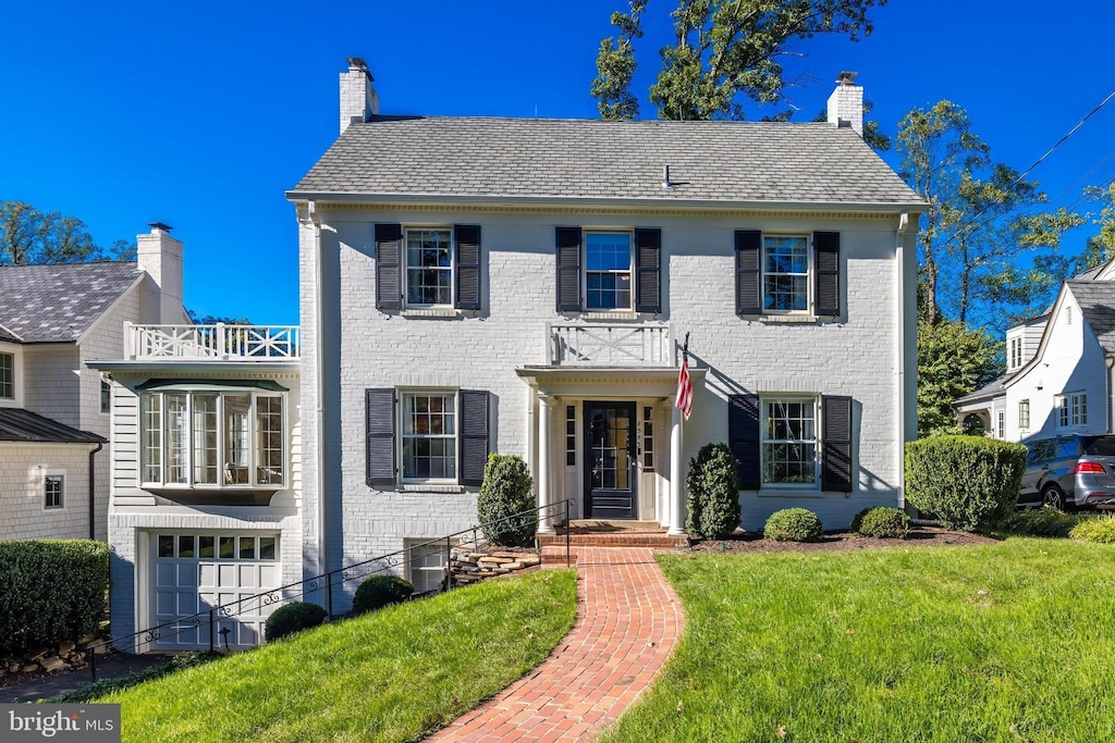 colonial house featuring a balcony, a front yard, and a garage