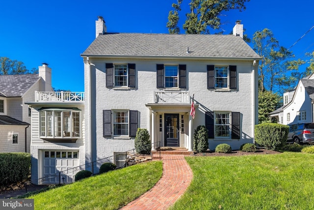 colonial house featuring a balcony, a front yard, and a garage