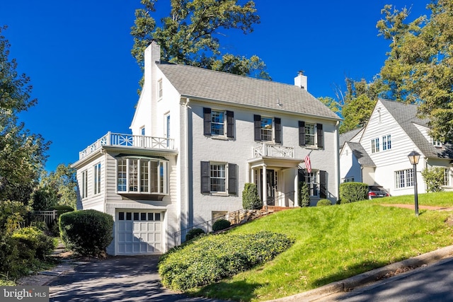 colonial inspired home featuring a balcony, a front yard, and a garage