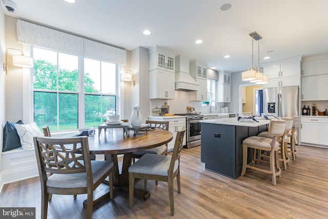 kitchen with pendant lighting, white cabinets, appliances with stainless steel finishes, a kitchen island, and custom range hood