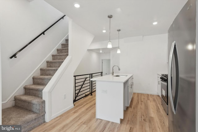 kitchen featuring stainless steel appliances, sink, pendant lighting, light hardwood / wood-style flooring, and an island with sink