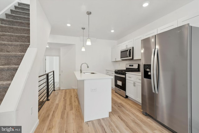 kitchen featuring a kitchen island with sink, white cabinets, sink, hanging light fixtures, and appliances with stainless steel finishes