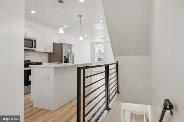 kitchen with light hardwood / wood-style floors, white cabinets, pendant lighting, and appliances with stainless steel finishes