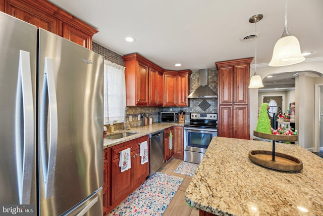 kitchen featuring appliances with stainless steel finishes, backsplash, light stone counters, wall chimney range hood, and decorative light fixtures