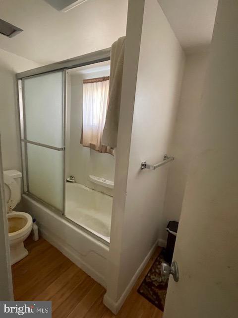 bathroom featuring hardwood / wood-style floors, shower / bath combination with glass door, and toilet