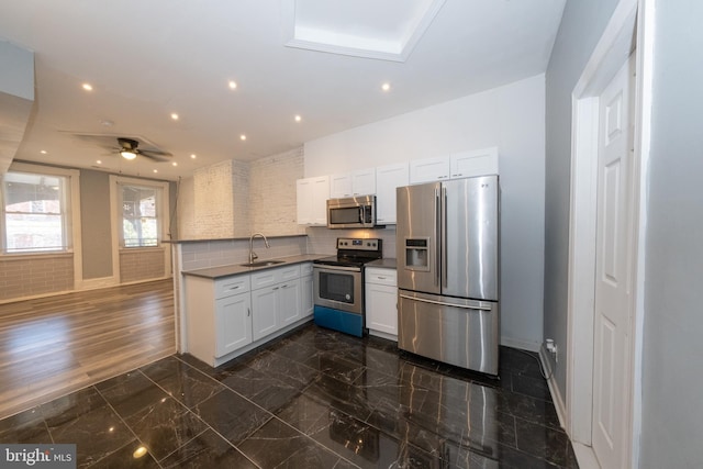 kitchen with decorative backsplash, stainless steel appliances, ceiling fan, sink, and white cabinets