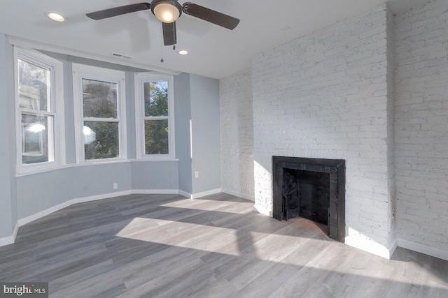 unfurnished living room featuring a fireplace, hardwood / wood-style flooring, ceiling fan, and brick wall