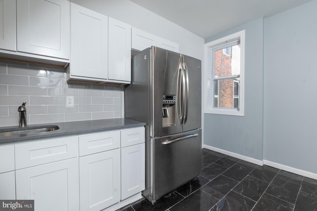 kitchen with backsplash, stainless steel fridge, white cabinetry, and sink