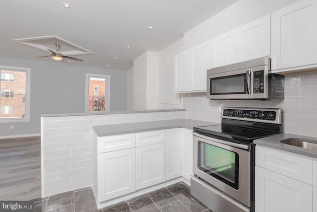 kitchen featuring kitchen peninsula, appliances with stainless steel finishes, decorative backsplash, dark hardwood / wood-style floors, and white cabinetry