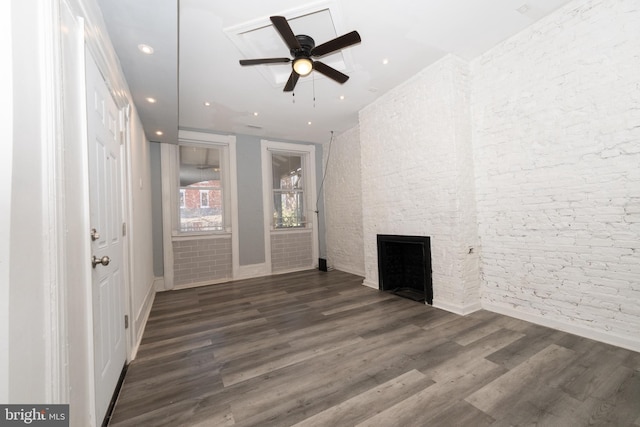 empty room with a fireplace, ceiling fan, dark wood-type flooring, and brick wall