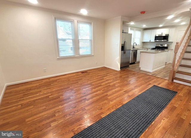 kitchen featuring white cabinetry, stainless steel appliances, crown molding, light hardwood / wood-style floors, and decorative backsplash