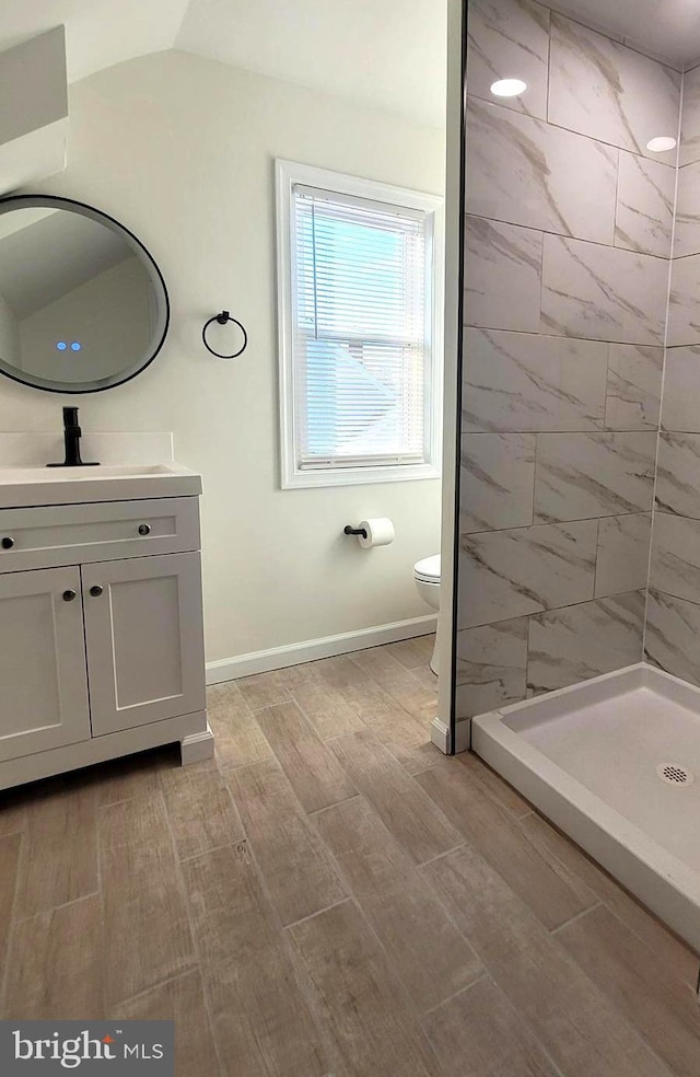 bathroom featuring vanity, vaulted ceiling, toilet, tiled shower, and wood-type flooring