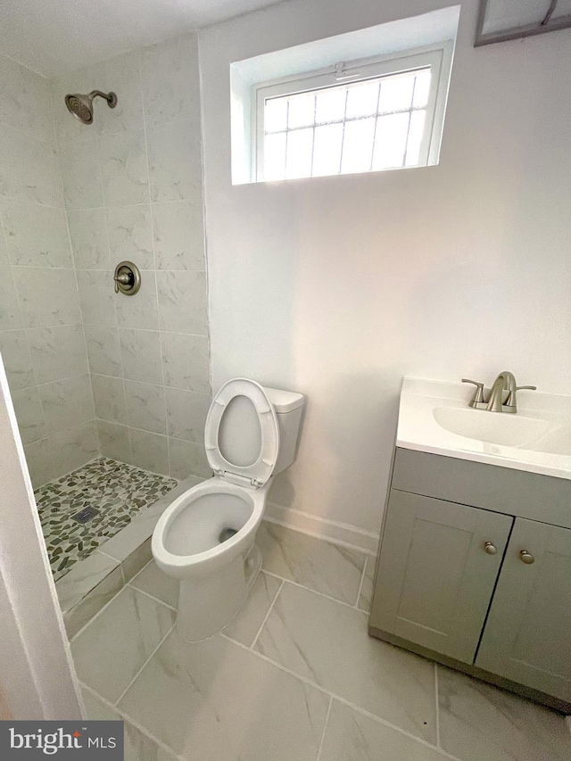 bathroom featuring a tile shower, vanity, and toilet