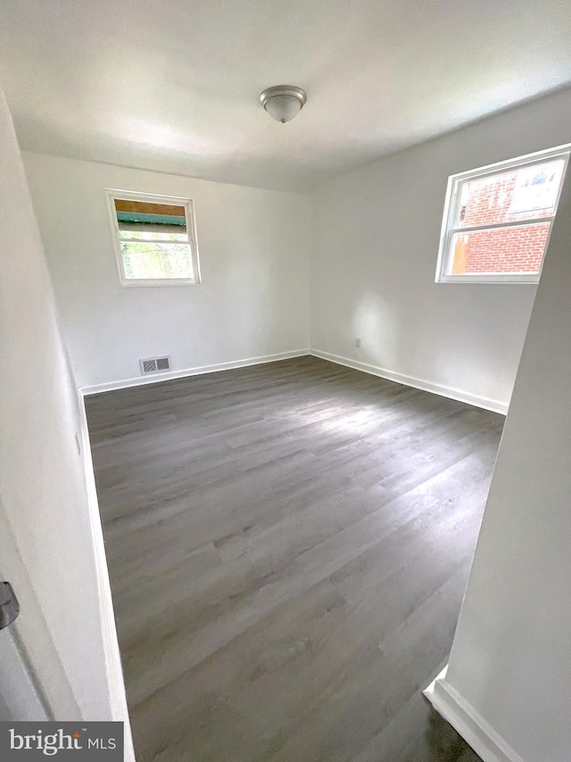 empty room with dark hardwood / wood-style flooring and plenty of natural light