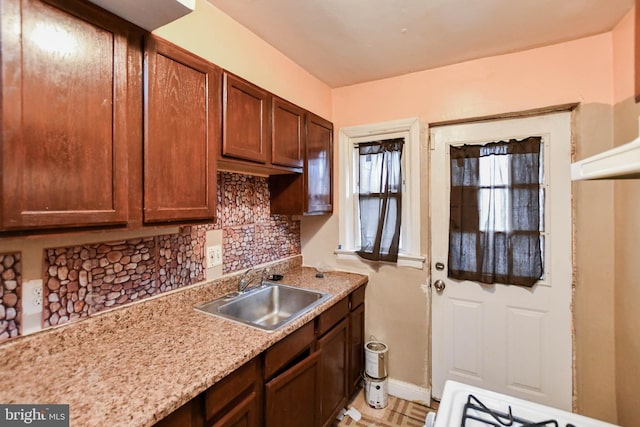 kitchen featuring stove, backsplash, light stone counters, and sink