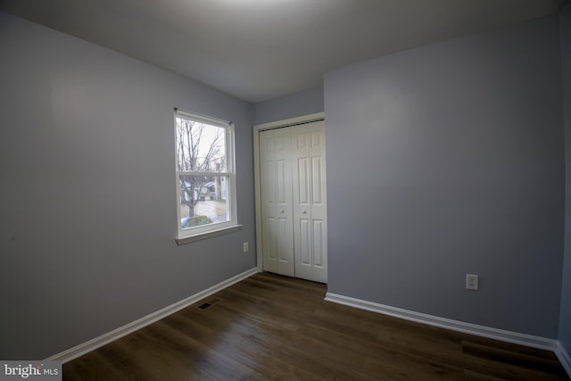 unfurnished bedroom featuring dark wood-style floors, a closet, visible vents, and baseboards