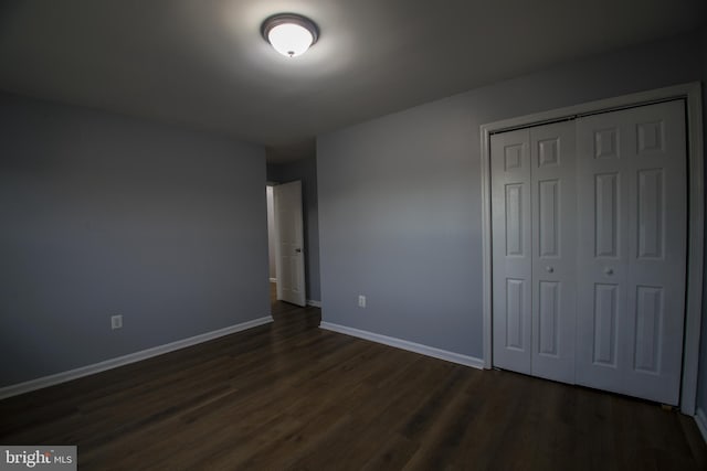 unfurnished bedroom featuring a closet, dark wood finished floors, and baseboards