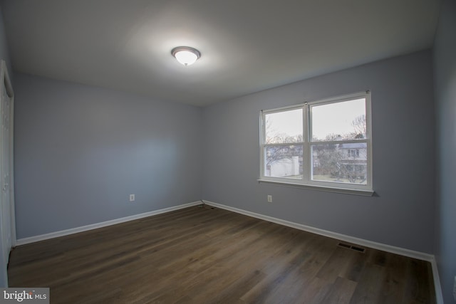 empty room featuring dark wood-style flooring, visible vents, and baseboards