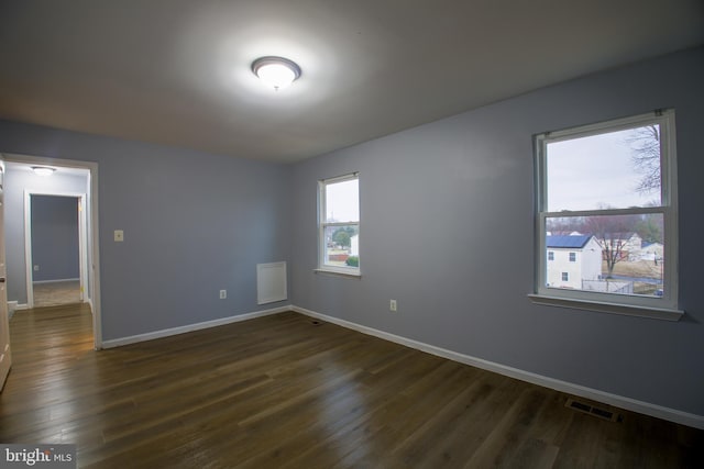 unfurnished room with dark wood-style flooring, visible vents, and baseboards