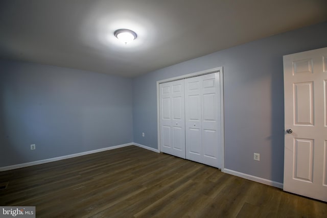 unfurnished bedroom featuring dark wood-style floors, visible vents, baseboards, and a closet