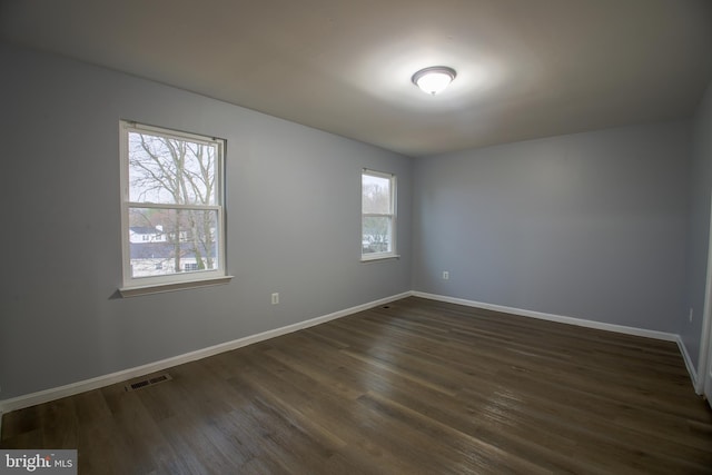 unfurnished room with dark wood-style flooring, plenty of natural light, visible vents, and baseboards