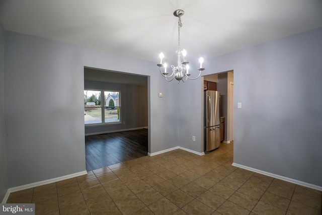 spare room with dark tile patterned flooring, a notable chandelier, and baseboards