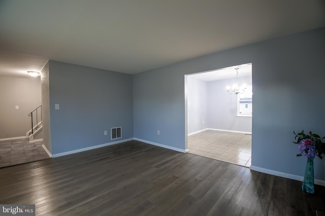 unfurnished room with baseboards, visible vents, dark wood finished floors, stairway, and a chandelier