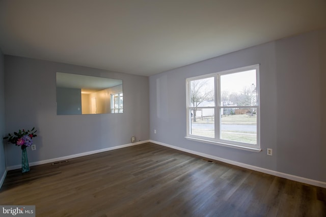 empty room featuring dark wood-style floors, visible vents, and baseboards