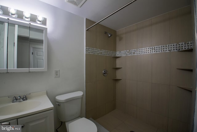 bathroom with toilet, visible vents, tiled shower, and vanity