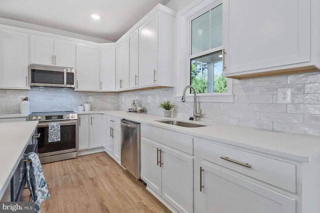 kitchen with white cabinets, sink, appliances with stainless steel finishes, tasteful backsplash, and light hardwood / wood-style floors