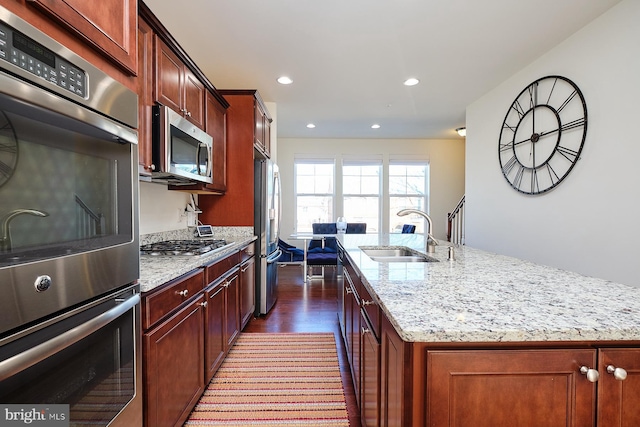 kitchen featuring light stone countertops, sink, dark wood-type flooring, a kitchen island with sink, and appliances with stainless steel finishes