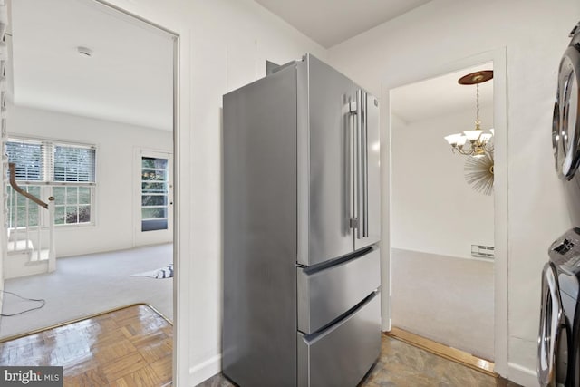 kitchen featuring stacked washer / dryer, high end refrigerator, parquet flooring, and an inviting chandelier