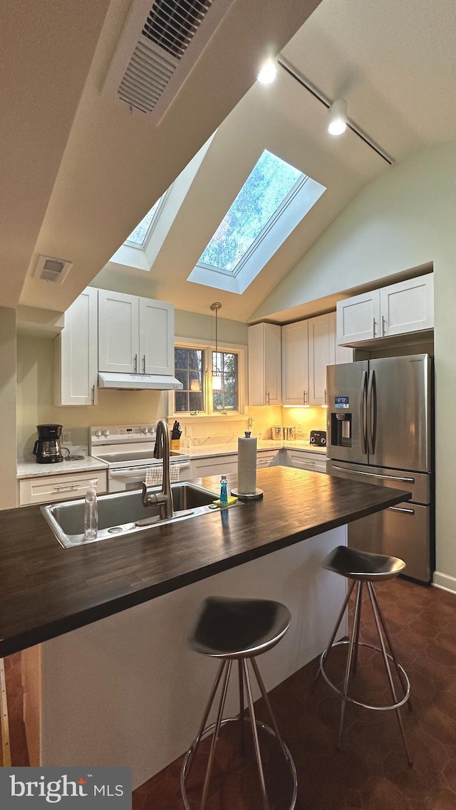 kitchen with butcher block countertops, a breakfast bar area, vaulted ceiling with skylight, white cabinets, and appliances with stainless steel finishes