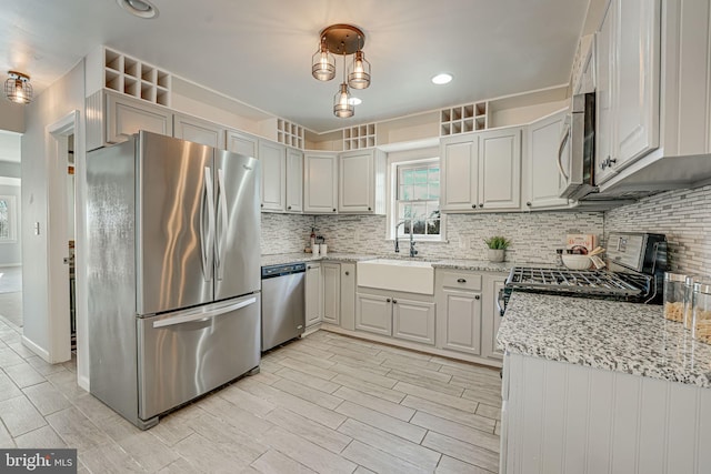 kitchen with pendant lighting, sink, decorative backsplash, light stone countertops, and stainless steel appliances