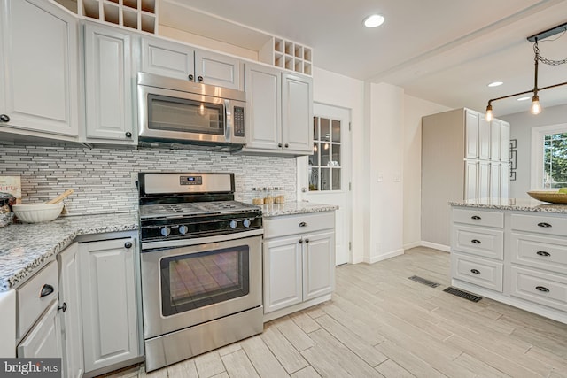 kitchen featuring appliances with stainless steel finishes, tasteful backsplash, decorative light fixtures, light stone counters, and white cabinetry