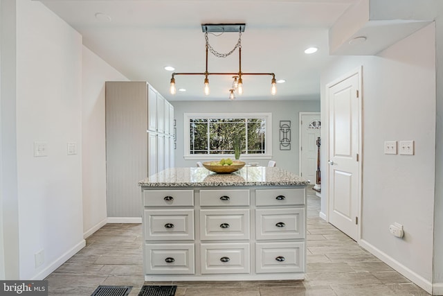 kitchen featuring a center island, light stone countertops, white cabinetry, and hanging light fixtures