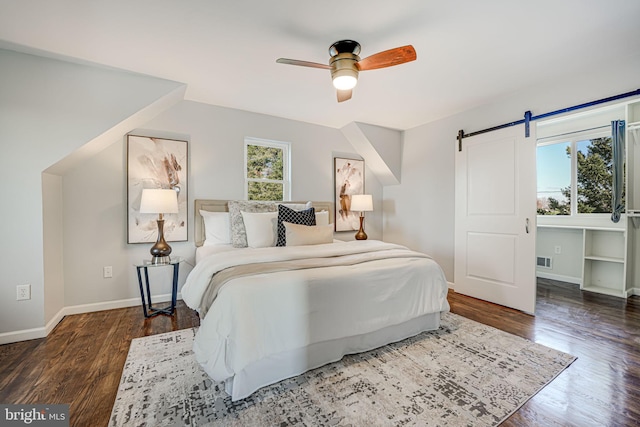 bedroom featuring ceiling fan, a barn door, and dark wood-type flooring