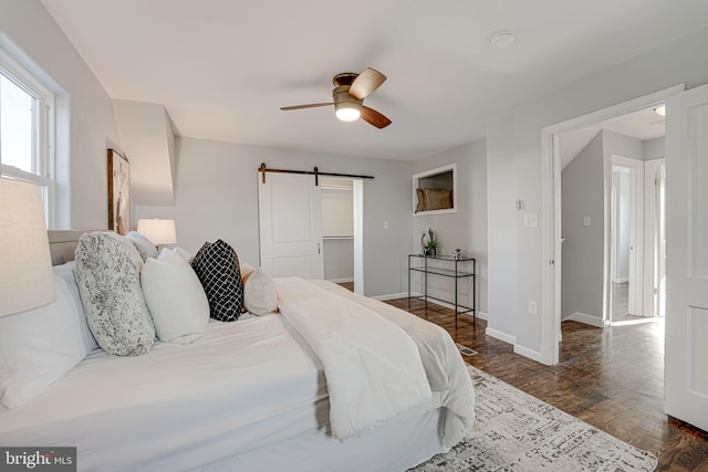 bedroom featuring ceiling fan, a barn door, dark hardwood / wood-style floors, a spacious closet, and a closet