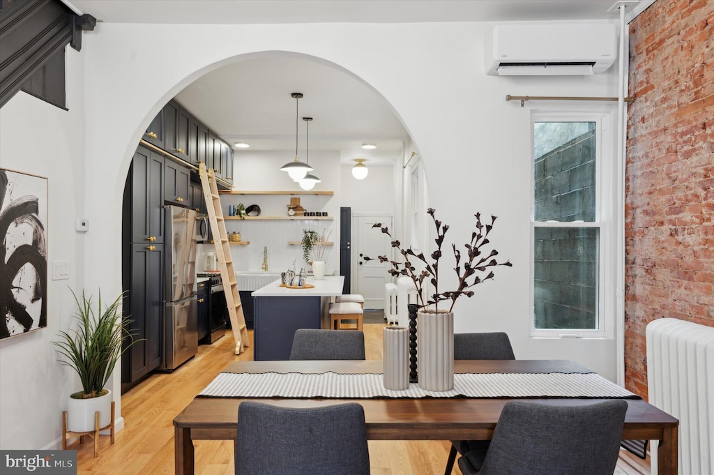 dining area with a wall mounted air conditioner, light hardwood / wood-style floors, radiator, and brick wall