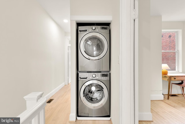 laundry area with stacked washer / drying machine and light wood-type flooring