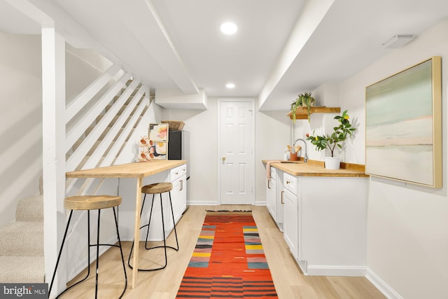 bar featuring sink, white cabinetry, light hardwood / wood-style flooring, and wooden counters