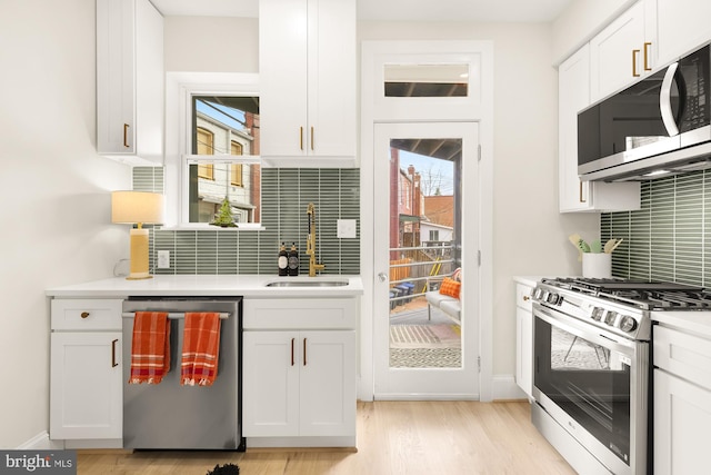 kitchen featuring backsplash, sink, appliances with stainless steel finishes, light hardwood / wood-style floors, and white cabinetry