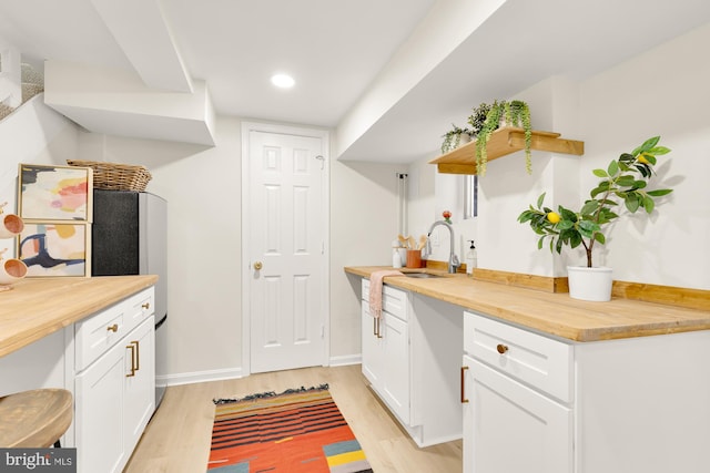 kitchen with butcher block countertops, sink, white cabinets, and light wood-type flooring