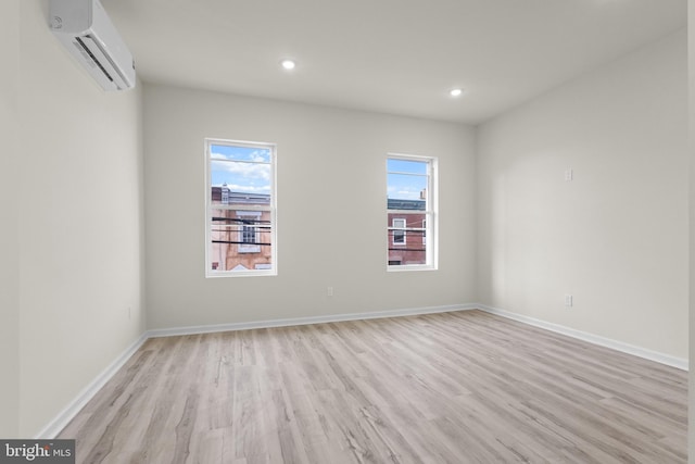 spare room featuring light wood-type flooring, an AC wall unit, and a healthy amount of sunlight