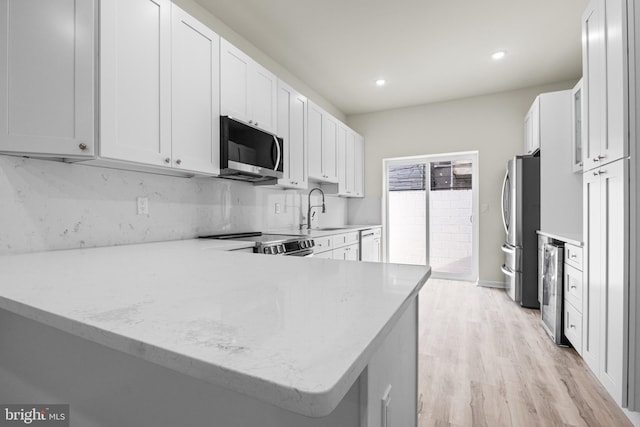 kitchen featuring kitchen peninsula, stainless steel appliances, white cabinetry, and light hardwood / wood-style floors