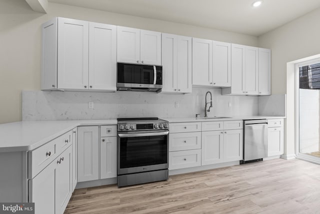 kitchen with white cabinetry, sink, stainless steel appliances, tasteful backsplash, and light wood-type flooring