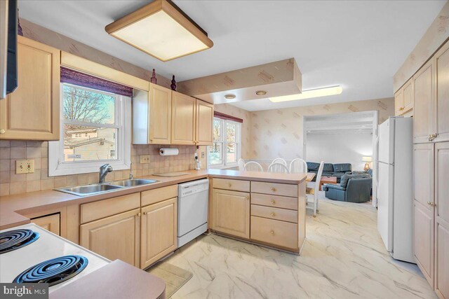 kitchen with backsplash, light brown cabinetry, sink, and white appliances