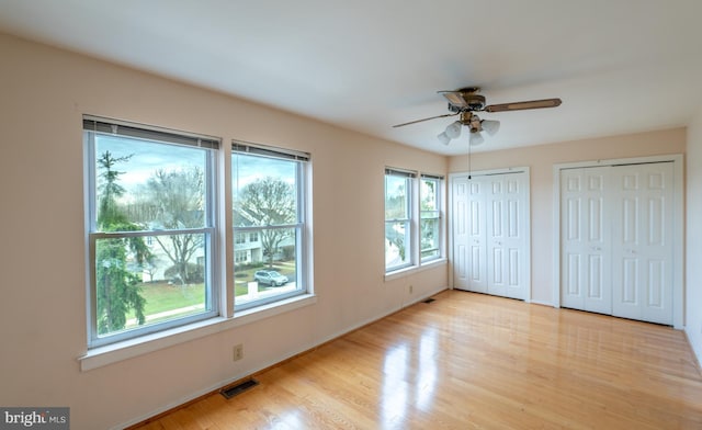 unfurnished bedroom featuring ceiling fan, light hardwood / wood-style floors, and two closets