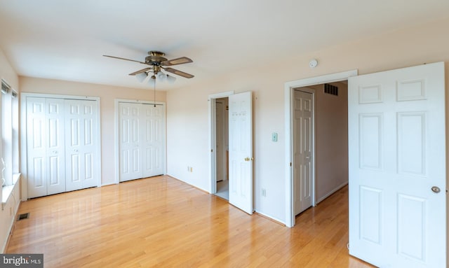 unfurnished bedroom featuring ceiling fan, light wood-type flooring, and multiple closets